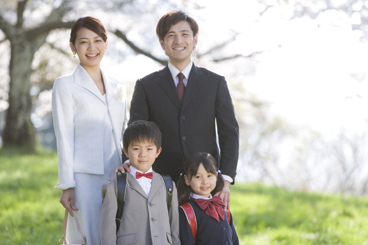 桜の下で、ダークスーツの父親と入学式に向かう家族